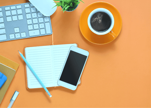 orange background with common items on a desk, coffee, keyboard, note pad, pen and cell phone