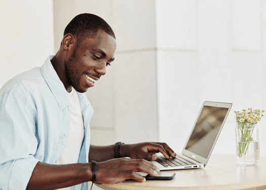A man smiling while he works at his desk on his laptop
