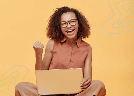 A girl siting cross legged with a laptop in her lap and cheering happily