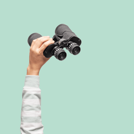 an arm holding up binoculars against a light green background