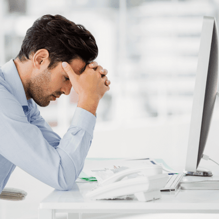 A msn sitting at a desk with his head resting in his hands looking defeated.