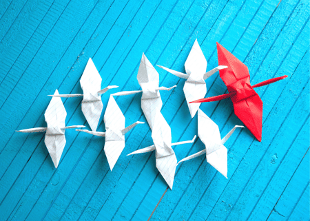 white paper cranes following a larger red paper crane