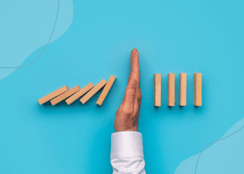 Blue background with a row of wood like dominoes falling on one another with a hand in the middle stopping them from all falling