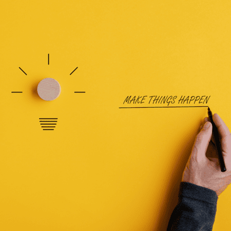 Yellow background with a light bulb and a hand writing the words "Make things happen"
